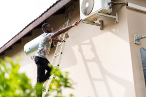 man on a ladder trying to reach his outside mini split unit